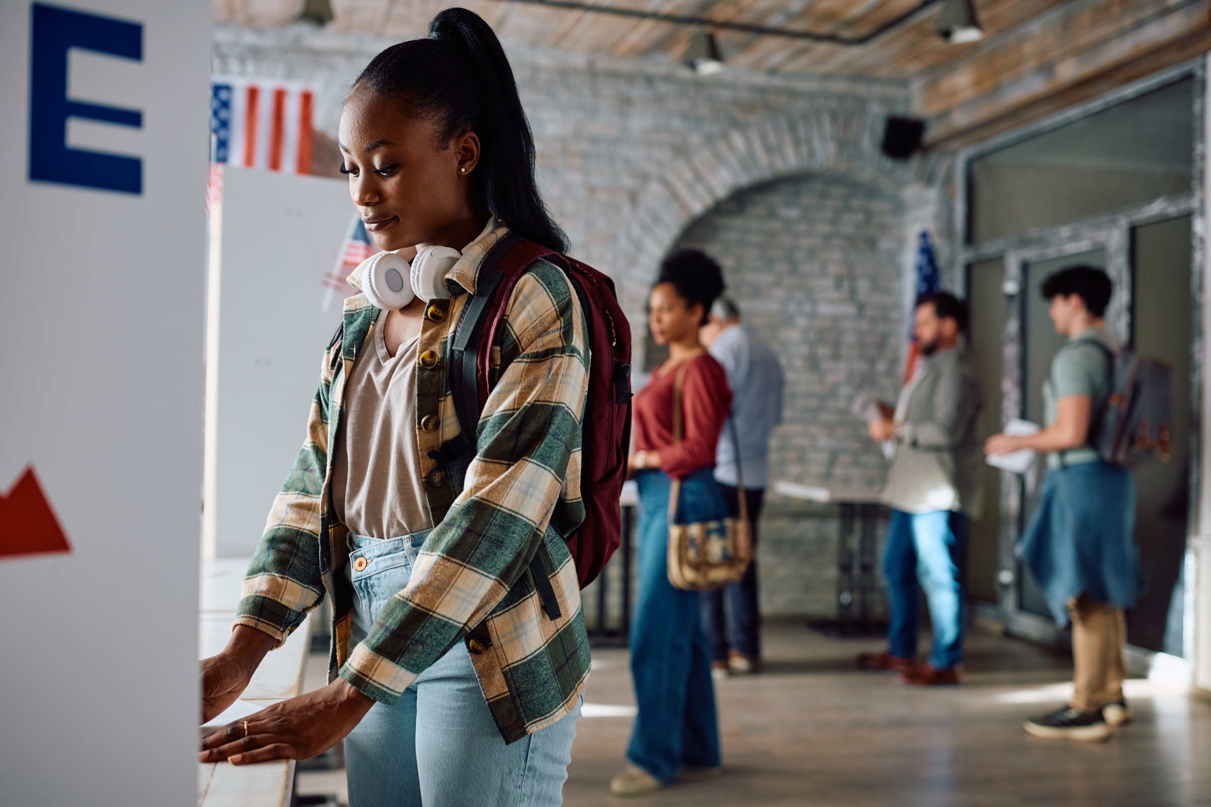 A young voter at a polling-place booth, with a line of other Milwaukee County voters waiting behind her.